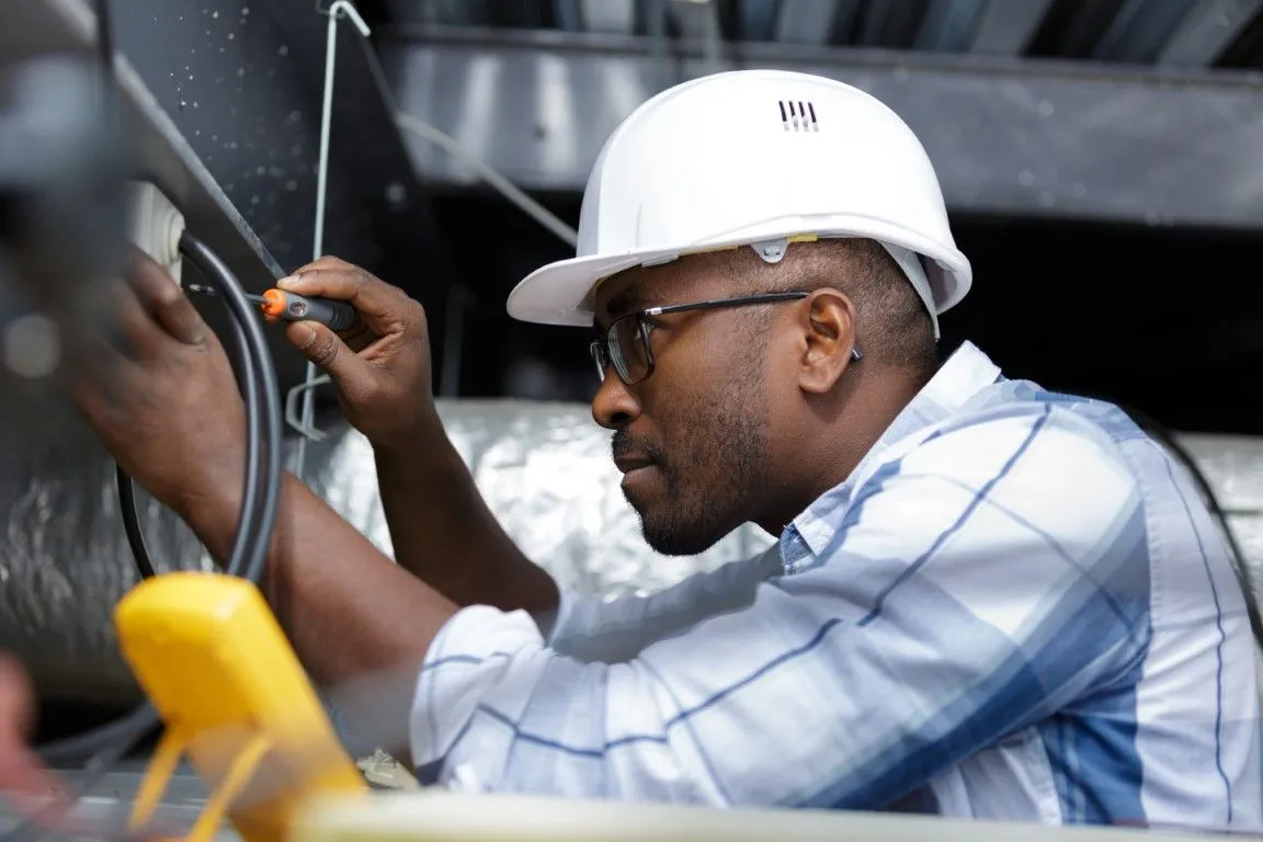 Worker in a white hard hat inspecting machinery with tools in an industrial setting